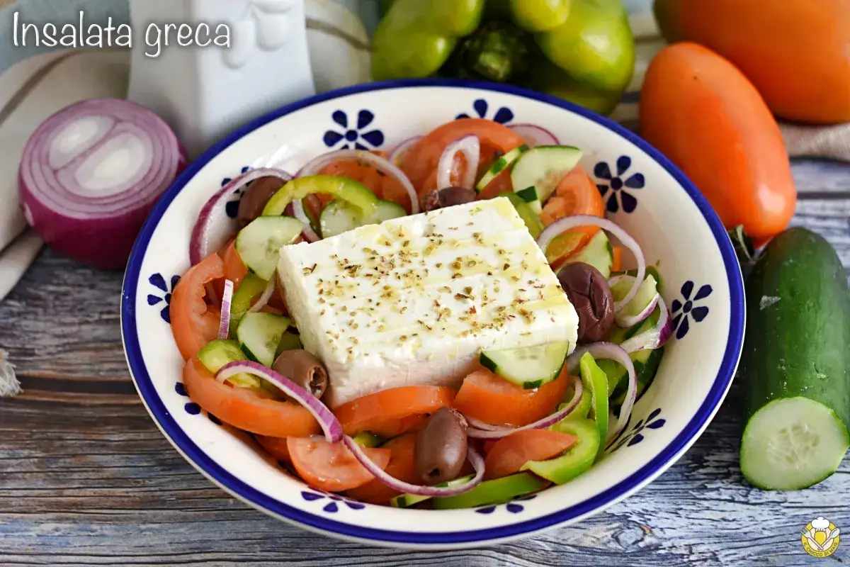 Insalata greca con un blocco di feta proprietà, pomodori, cetrioli, cipolla rossa, peperoni verdi e olive nere.