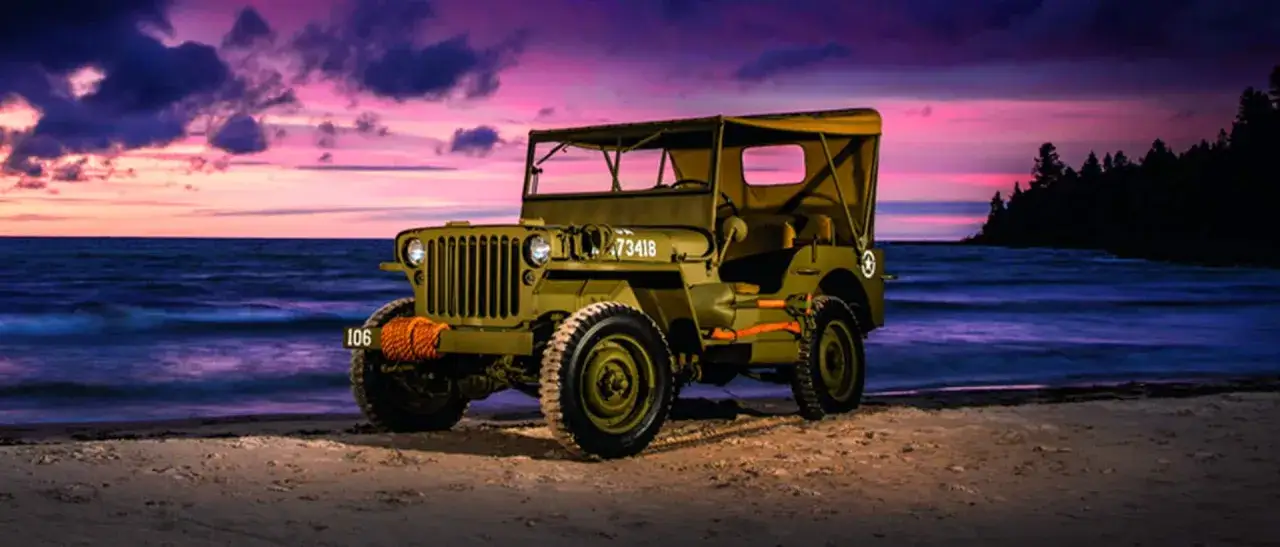 Zielony jeep, symbol amerykańskiej motoryzacji, stoi na plaży o zachodzie słońca.