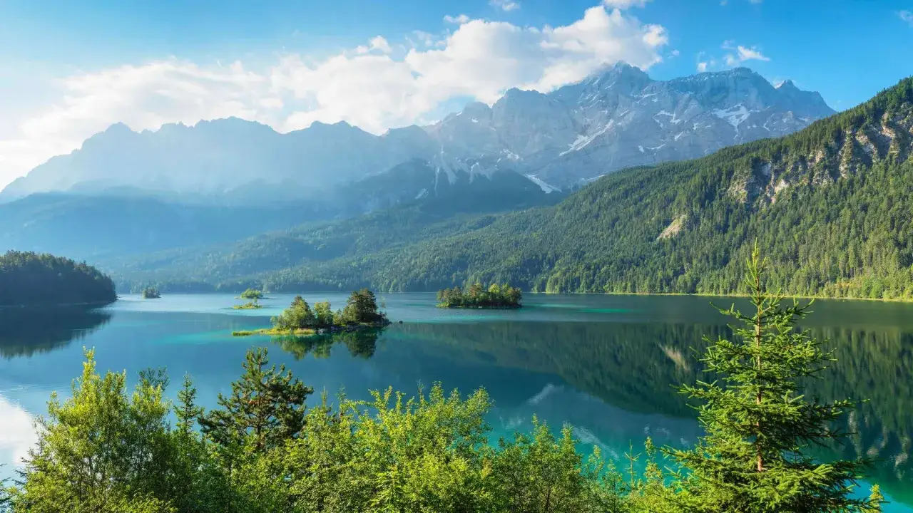 T&uuml;rkisblauer See mit kleinen Inseln, umgeben von gr&uuml;nen W&auml;ldern und majest&auml;tischen Bergen. Perfekt f&uuml;r eine leichte Wanderung.
