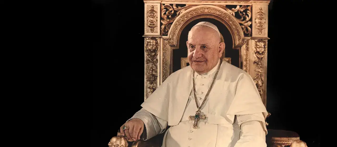 Papst Johannes XXIII. sitzt in einem prunkvollen Thron, trägt ein weißes Gewand und eine goldene Kette mit Kreuz.