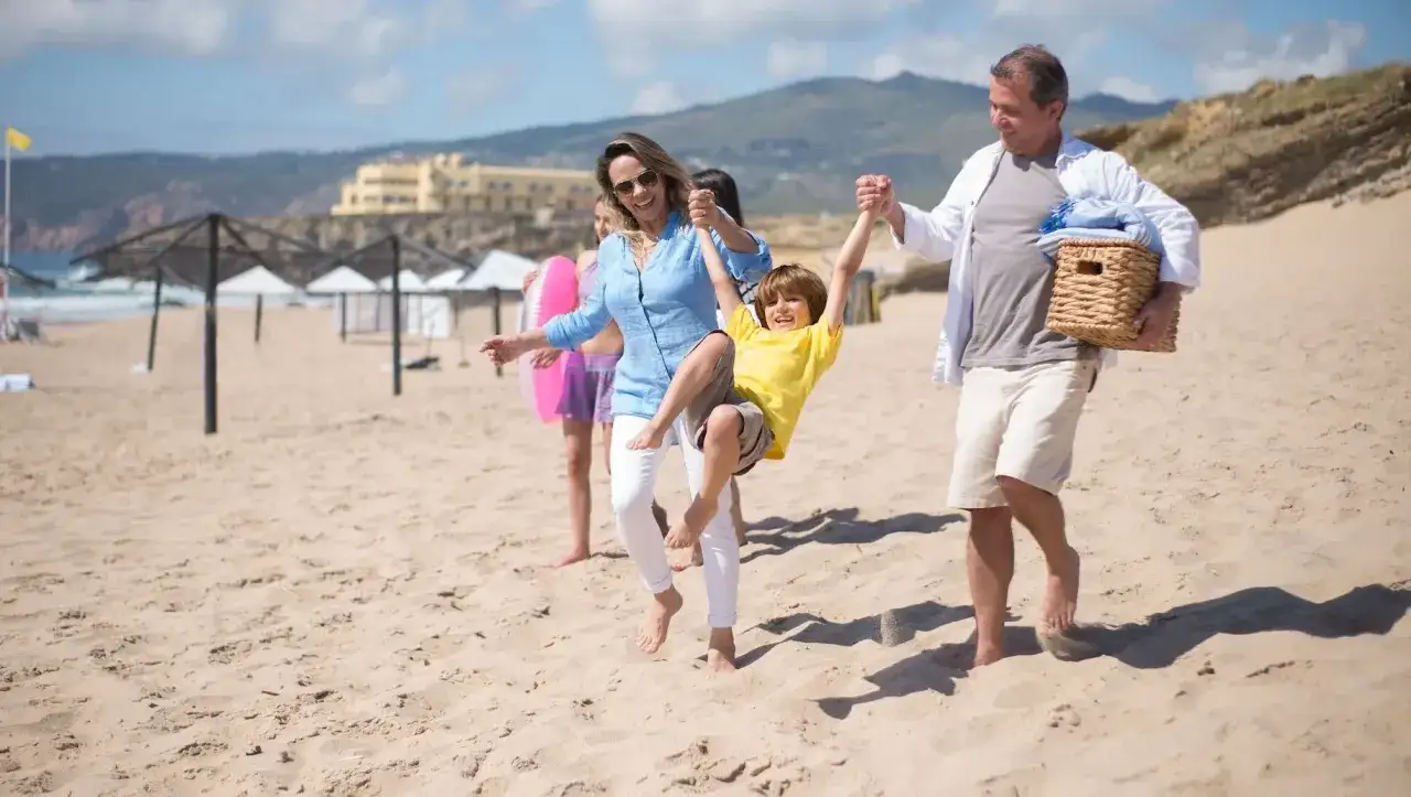 Rodzina cieszy się wakacjami na raty na piaszczystej plaży. Ojciec niesie koszyk, matka bawi się z synem.