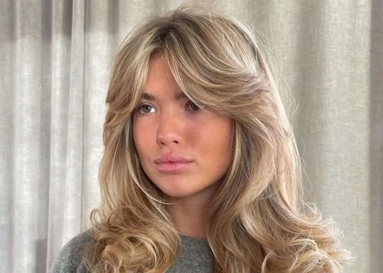 Kobieta z blond włosami i grzywką w stylu scandi hairline, ułożoną na boki, z delikatnymi falami.