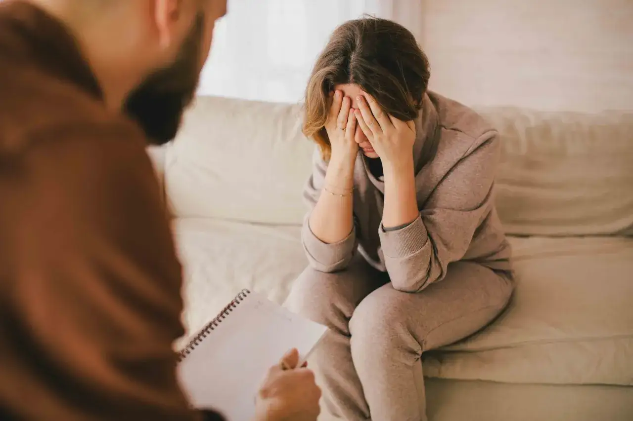 Una donna piange, coprendosi il viso con le mani, mentre parla con un terapeuta. Si interroga su quanto tempo portare il lutto.