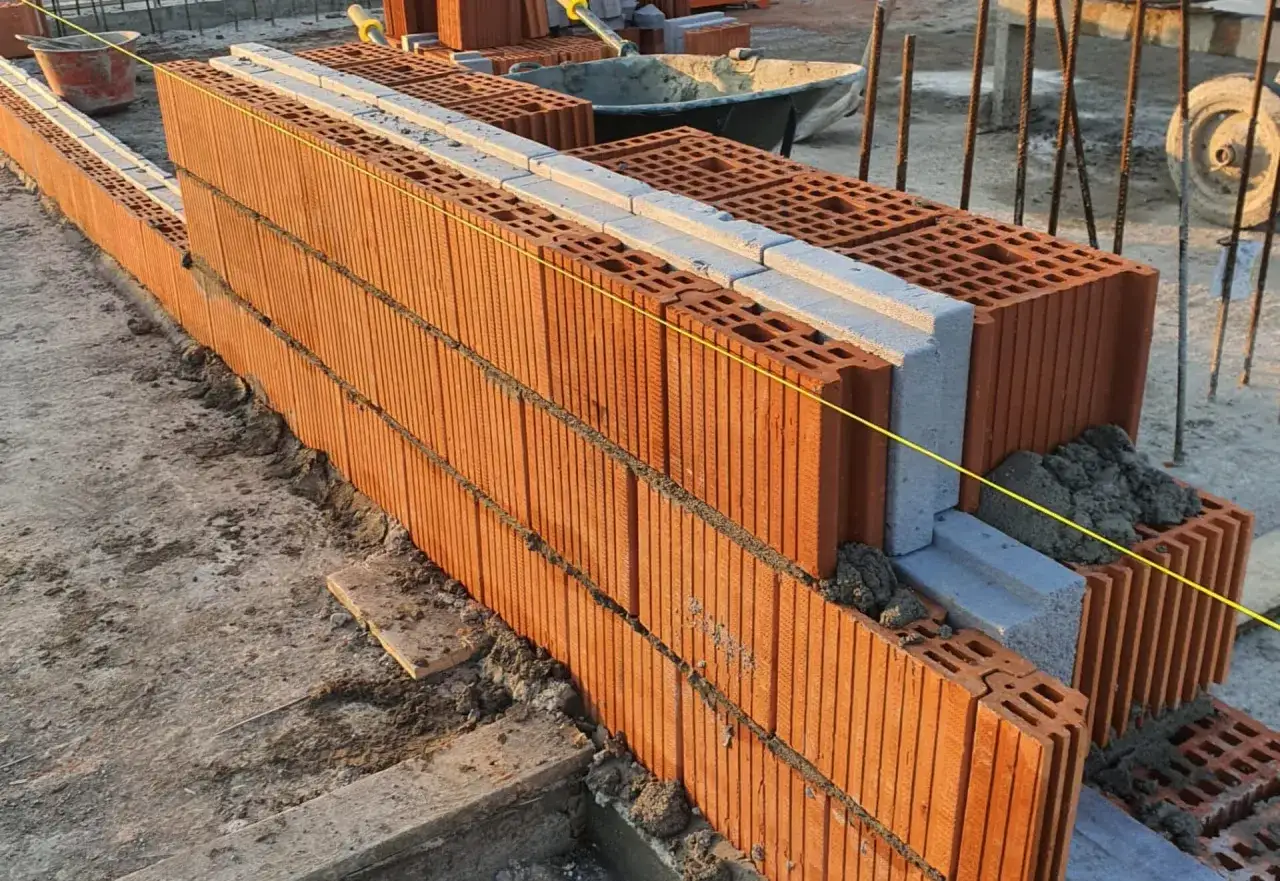 Muro in costruzione con blocchi di laterizio e isolante. La **trasmittanza lana di roccia 10 cm** è un fattore chiave per l'efficienza energetica.