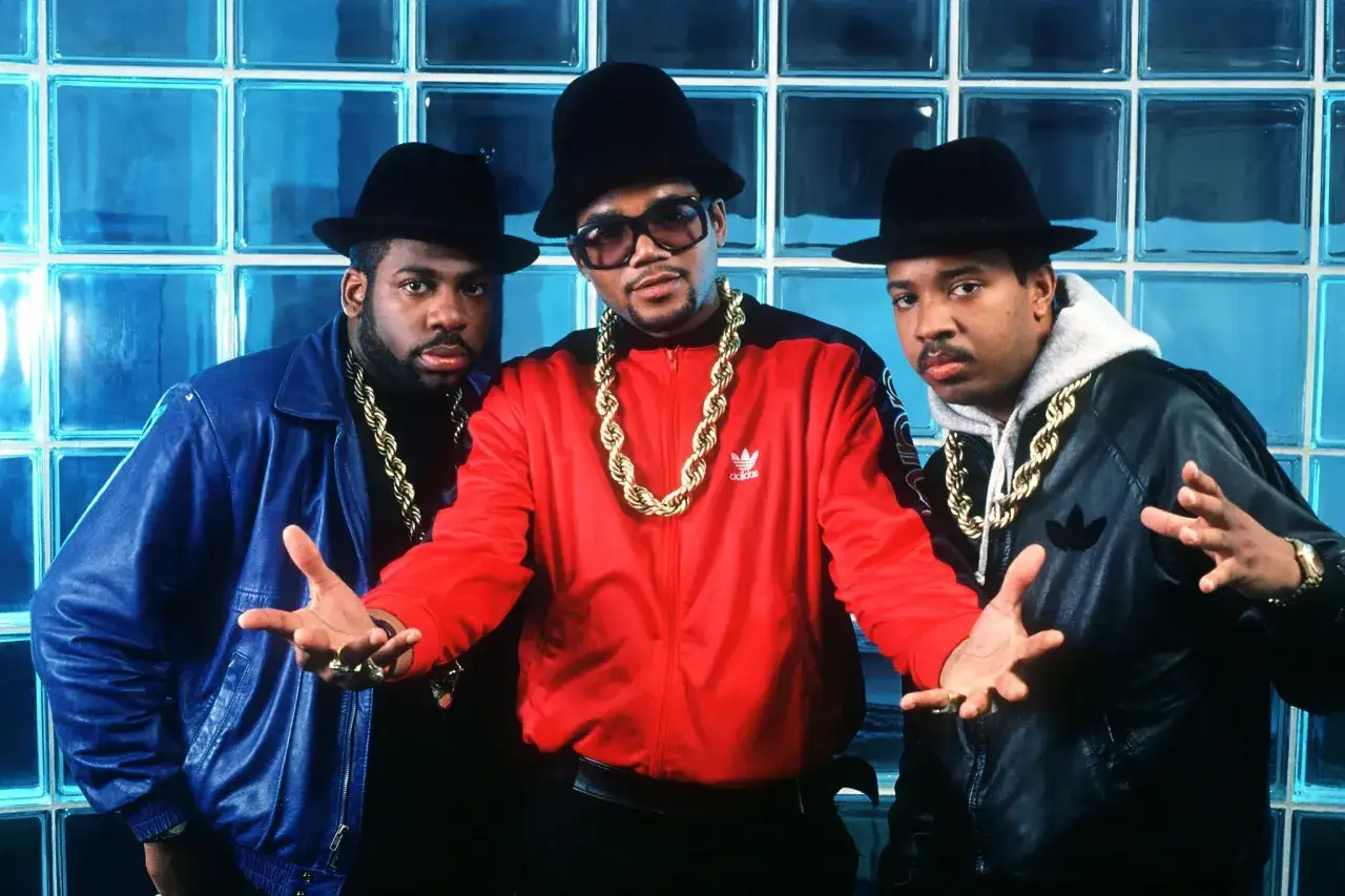 Trois rappeurs portent des chapeaux et des chaînes en or. L'un d'eux, au centre, pourrait être le premier rappeur français.