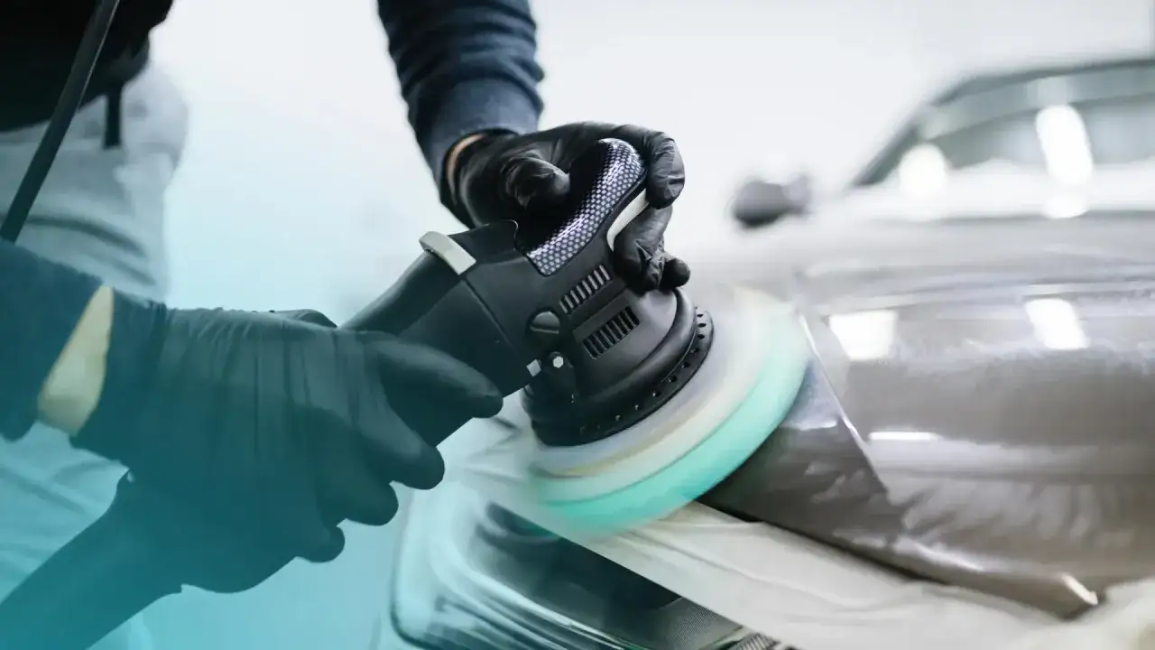 Gloved hands use a buffer to polish a car's headlight, revealing a smooth, shiny finish. This demonstrates how to polish a car with a buffer for a showroom look.