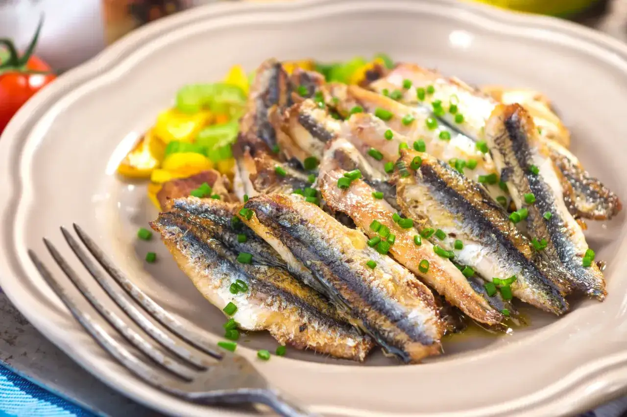Piatto di alici alla scapece, dorate e croccanti, guarnite con erba cipollina e accompagnate da verdure miste.