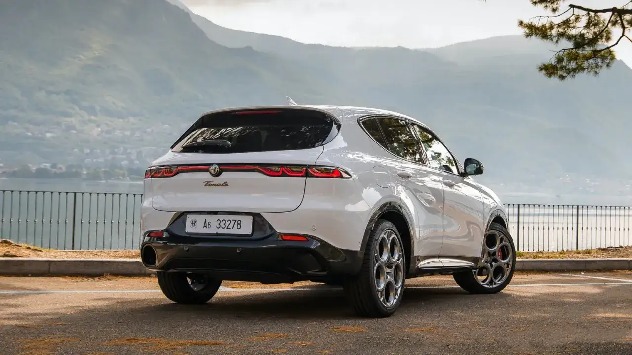 Białe Alfa Romeo Tonale z pięknymi felgami, zaparkowane nad jeziorem. Sprawdź aktualną alfa romeo tonale cena i wybierz swój wymarzony model.