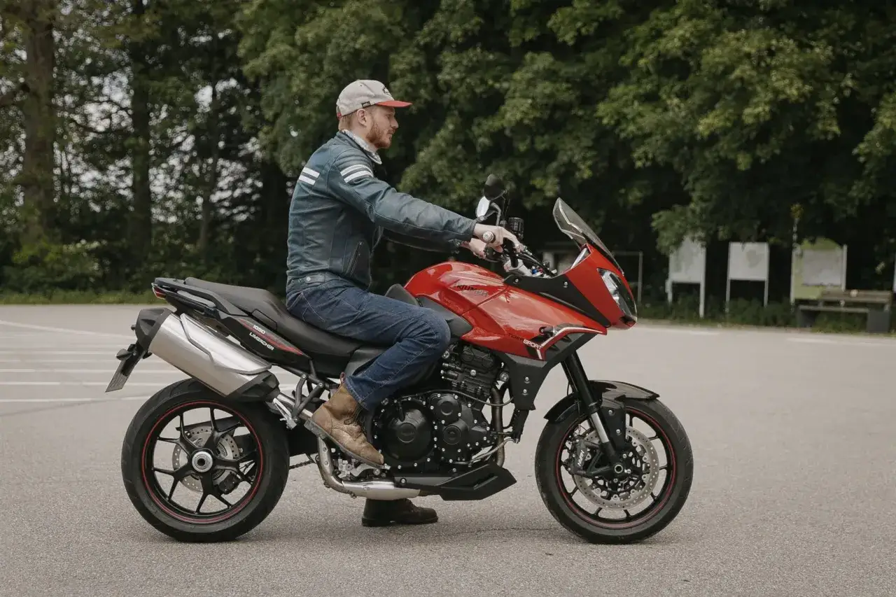 Mężczyzna na czerwonym motocyklu Triumph Tiger 1050. Poznaj jego dane techniczne i poczuj wolność na drodze.