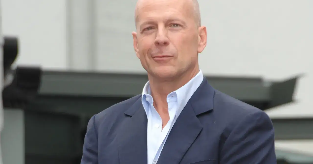 Bruce Willis, żyje i ma się dobrze, pozuje w granatowej marynarce i błękitnej koszuli.