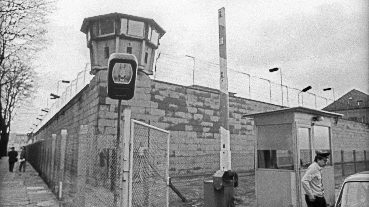Wachturm und Grenzmauer der deutschen demokratischen Republik. Ein Grenzsoldat steht an einem Kontrollpunkt.
