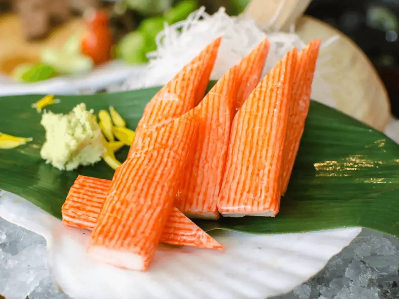 Pomarańczowe paluszki surimi, idealne na przekąskę w ciąży, podane na liściu z wasabi i ozdobami.