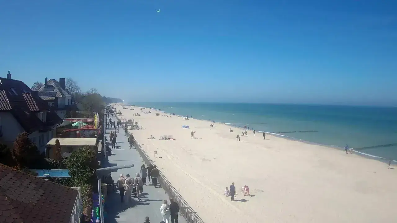 Spacer w Sarbinowie z widokiem na plażę i morze. Ludzie spacerują, bawią się na piasku. To świetne **sarbinowo atrakcje** dla każdego.
