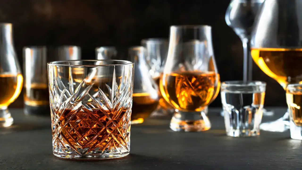 Szklanki z bursztynowym trunkiem, w tym jedna z kryształowym zdobieniem. Różnice między koniakiem a whisky mogą być subtelne, ale smak i aromat są kluczowe.