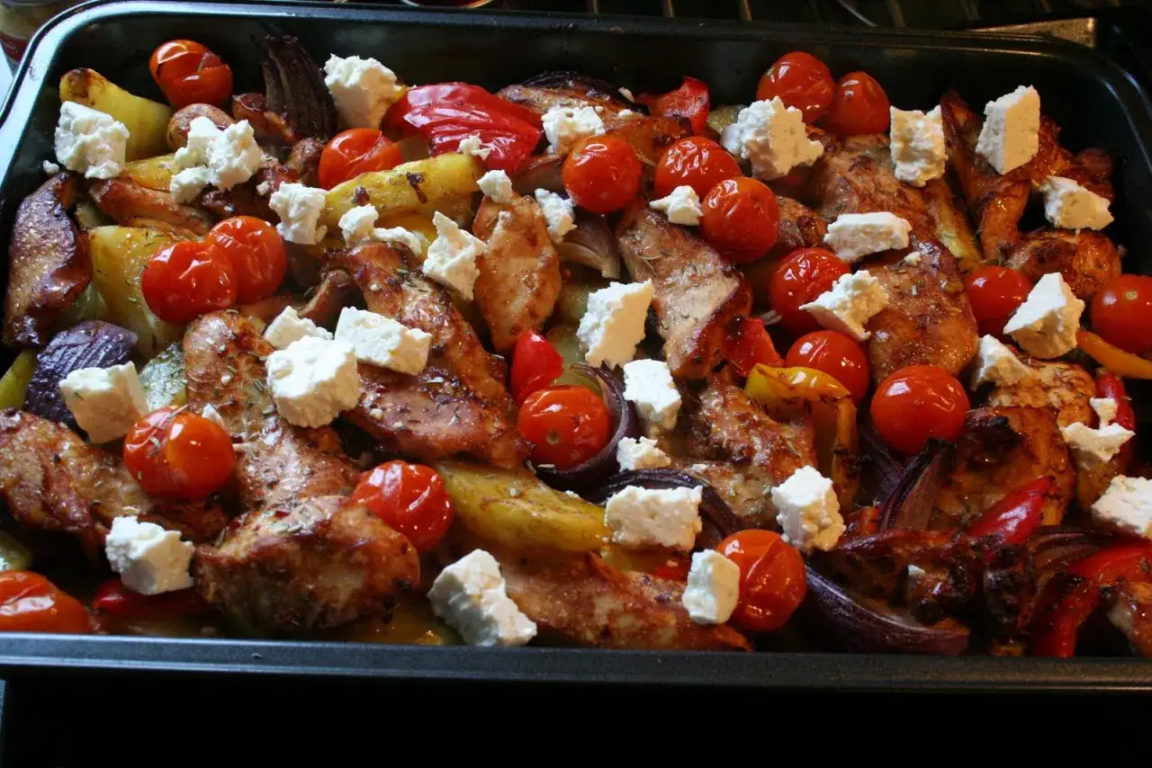 En h&auml;rlig grekisk pyttipanna med kyckling, potatis, tomater och fetaost i en ugnsform.