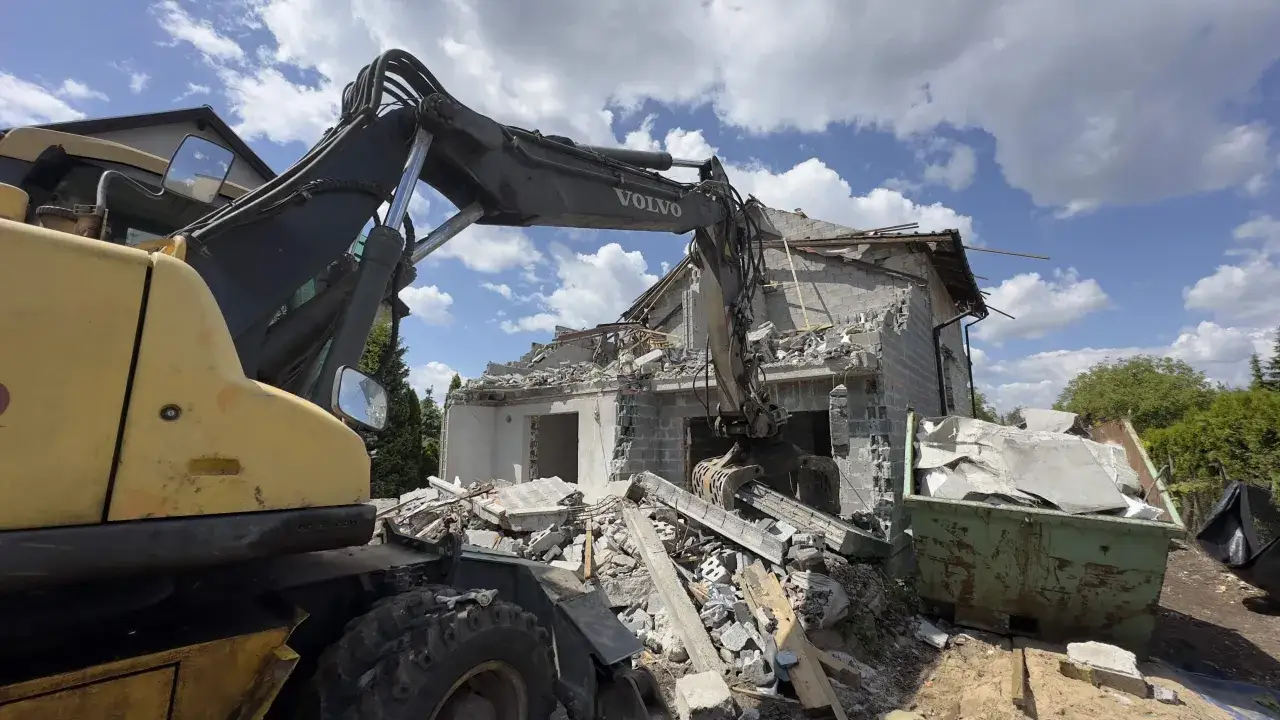 Koparka Volvo pracuje przy wyburzeniu domu. Gruz trafia do kontenera. Poznaj wyburzenie domu koszt.