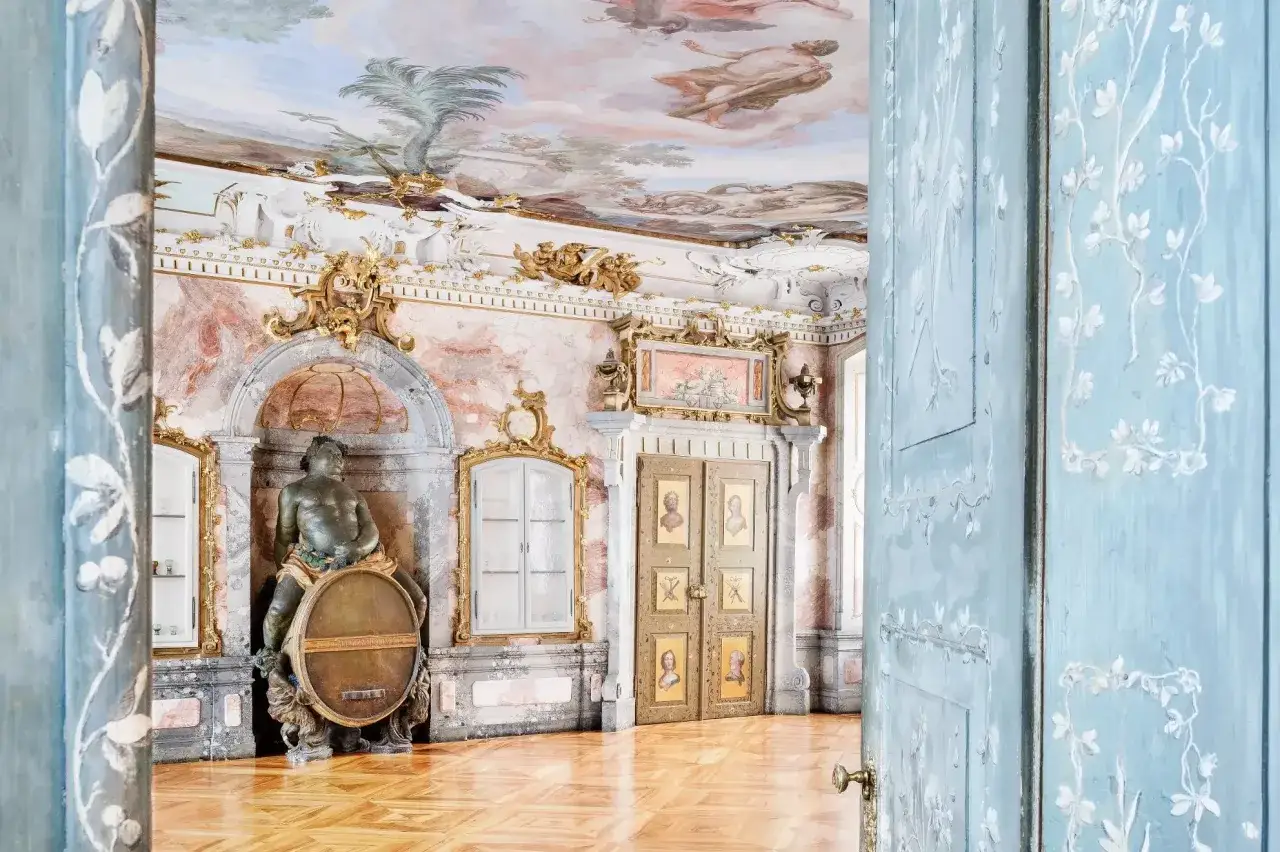 Prunkvoller Raum im neuen Schloss Tettnang mit Deckenmalerei, Marmorw&auml;nden, einer Statue und bemalten T&uuml;ren.