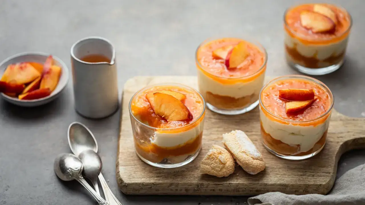 Delizioso tiramis&ugrave; alle pesche in coppette, guarnito con pesche fresche e accompagnato da savoiardi.