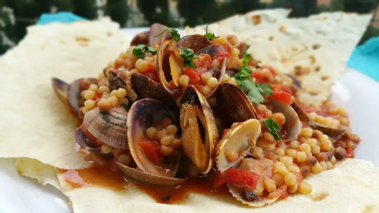 Un piatto di fregola con arselle, pomodoro e prezzemolo, un classico da provare per scoprire cosa mangiare in Sardegna.