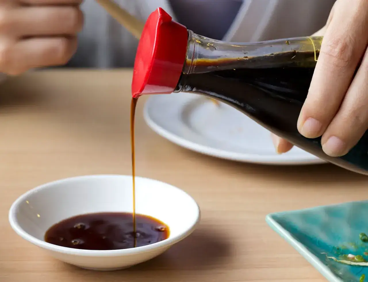 Dłoń przelewa sos sojowy do małej miseczki, idealny dodatek do sushi i innych azjatyckich potraw.