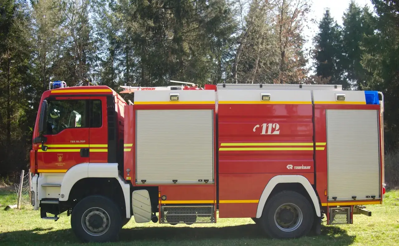Czerwony wóz strażacki z numerem 112, gotowy do akcji. Brygadier czuwa nad bezpieczeństwem.