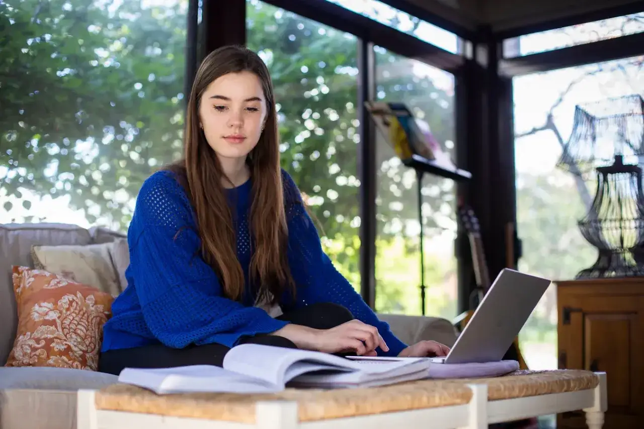 A young woman studies for her MPA online, researching the best online mpa programs from her laptop in a sunlit room.