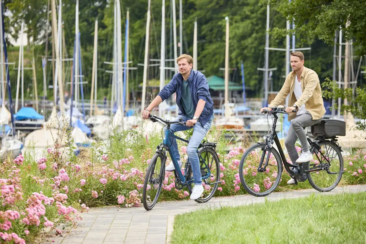 Zwei M&auml;nner genie&szlig;en eine Fahrradtour in Haltern am See, vorbei an bl&uuml;henden Rosen und Segelbooten.