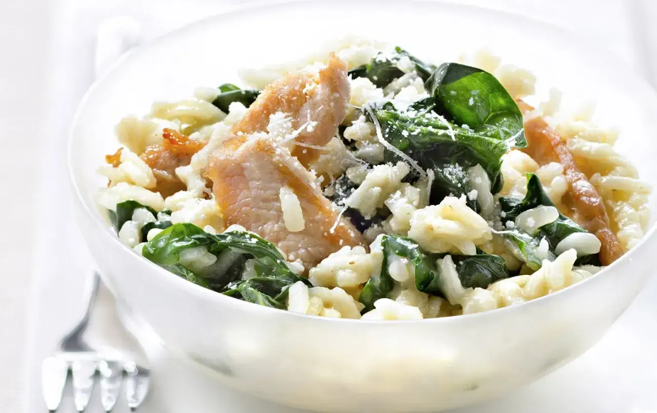 Un délicieux risotto aux épinards et poulet, parsemé de parmesan râpé, servi dans un bol blanc.