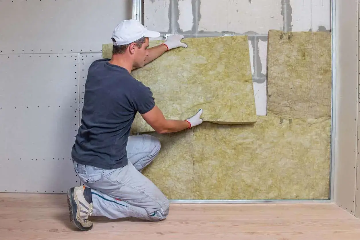 Un ouvrier installe un isolant pour éviter l'effet paroi froide. La laine minérale est posée sur un mur en construction.