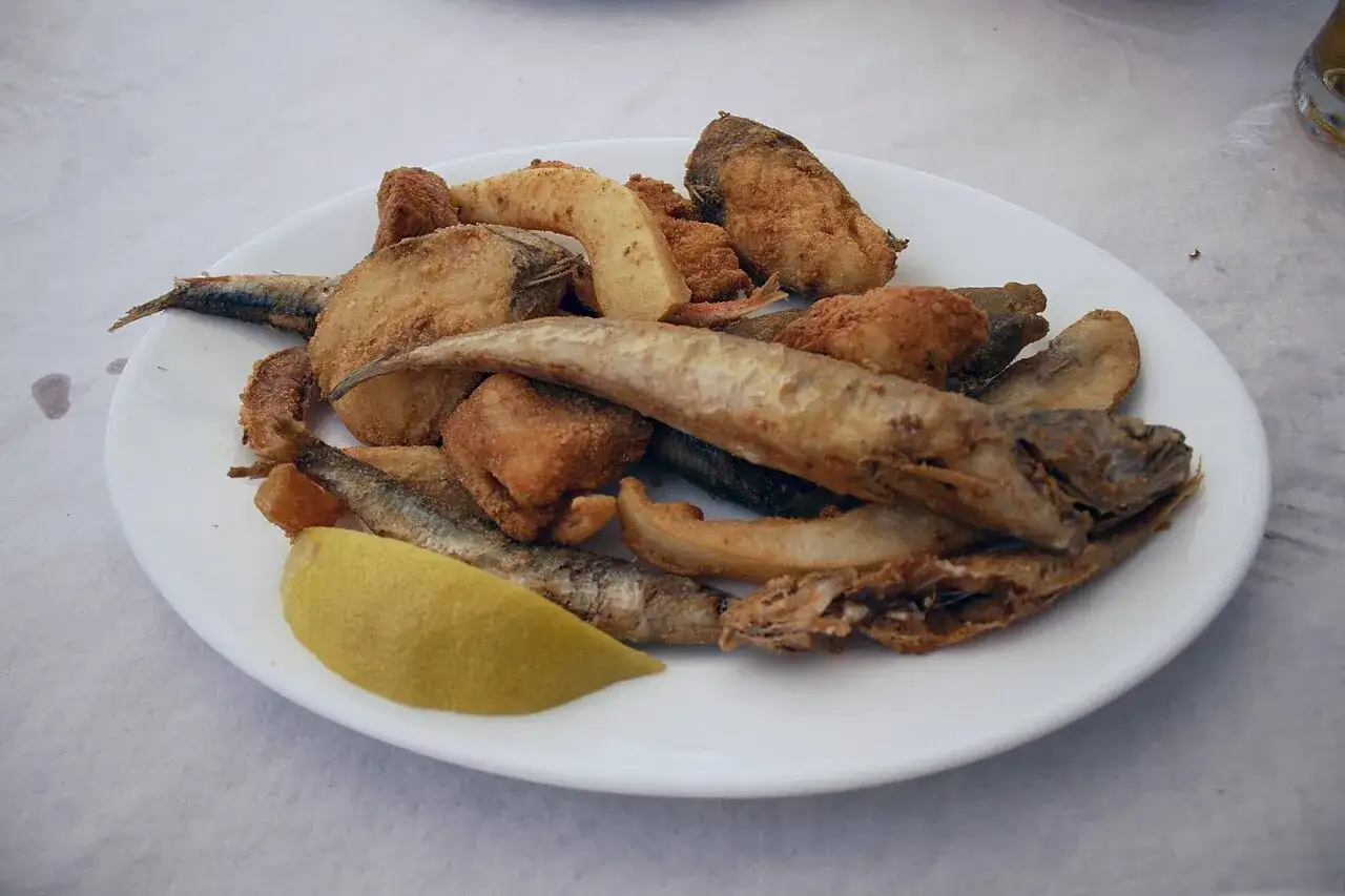 Plato de boquerones fritos y trozos de pescado rebozado, con una rodaja de limón.