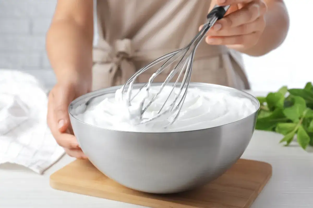 Mani che montano la panna in una ciotola d'acciaio, pronta per essere gustata.