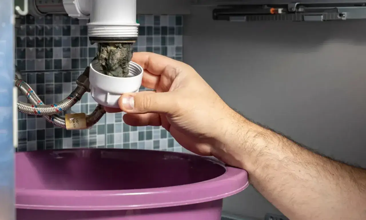 Main tenant retire un bouchon de siphon plein de débris pour déboucher la canalisation.