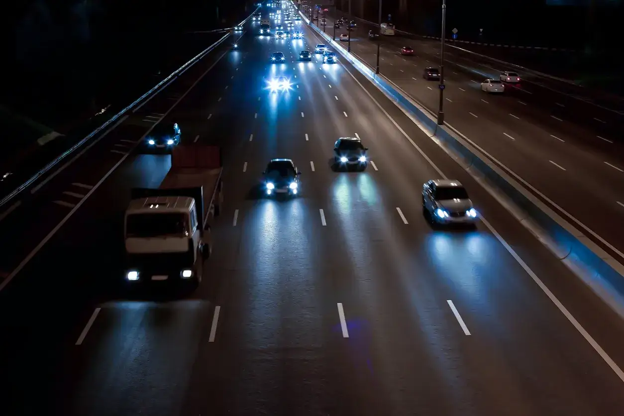 La nuit, les feux de route éclairent la distance sur cette autoroute où circulent camions et voitures.