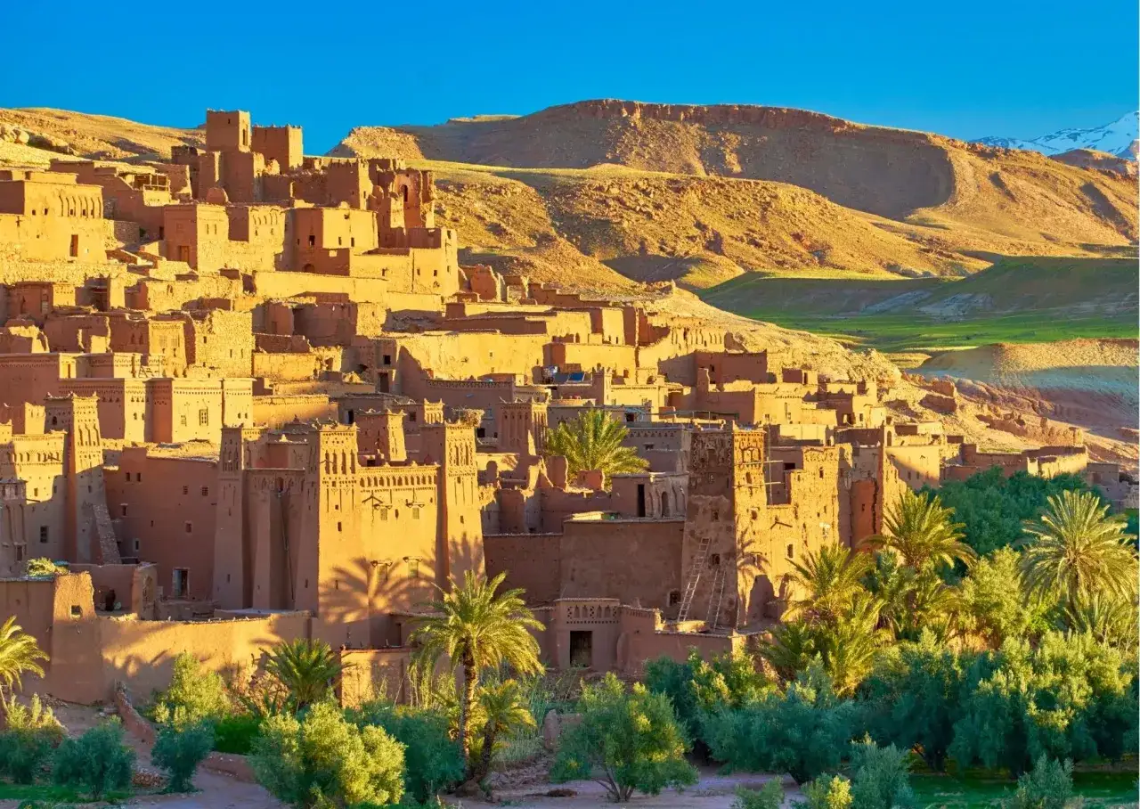 Village fortifi&eacute; en terre ocre, A&iuml;t Benhaddou, Maroc. Id&eacute;al pour une randonn&eacute;e Atlas Maroc, avec des palmiers et des montagnes en arri&egrave;re-plan.