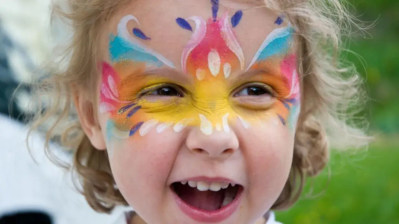 Ni&ntilde;a con cara pintada de colores vibrantes, lista para el carnaval. Su sonrisa contagiosa y el maquillaje festivo la hacen lucir como una peque&ntilde;a mariposa.