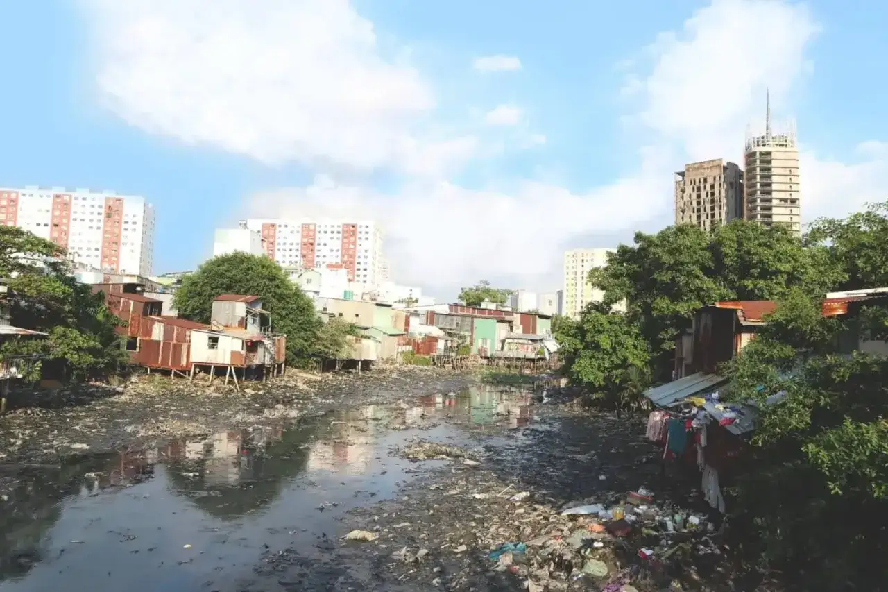Río contaminado con basura y casas precarias, reflejo de las causas de la contaminación del aire y del agua.