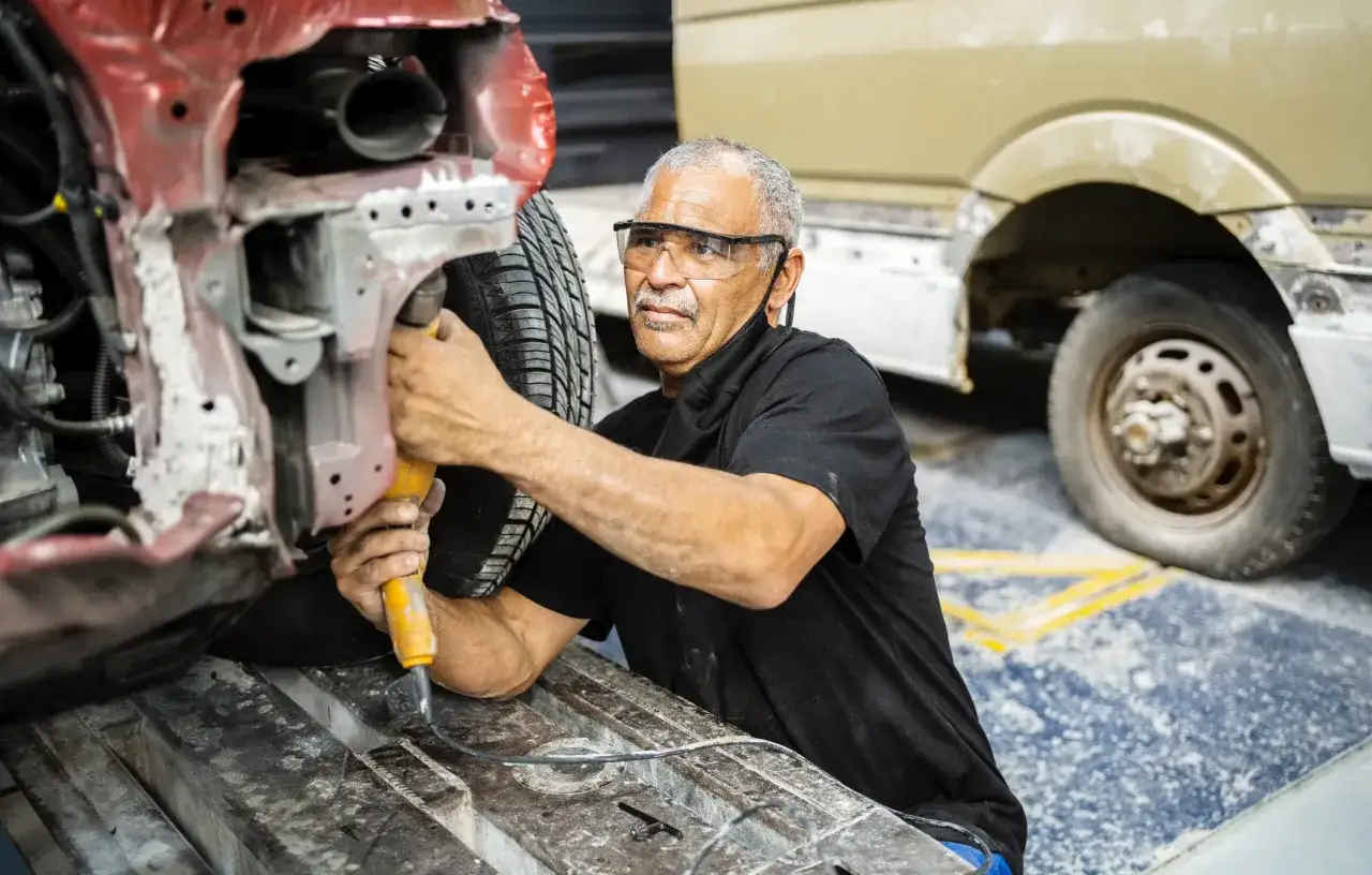 Mechanik w okularach ochronnych pracuje przy samochodzie. Wymiana podłużnicy cena może być różna, zależy od uszkodzeń.