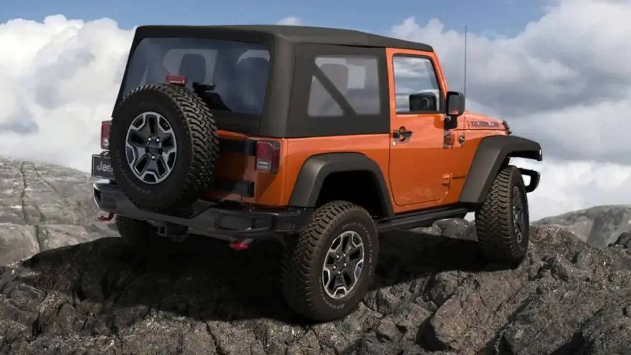 Jeep naranja Rubicon, listo para la aventura offroad que es su destino, superando rocas con sus robustas llantas.