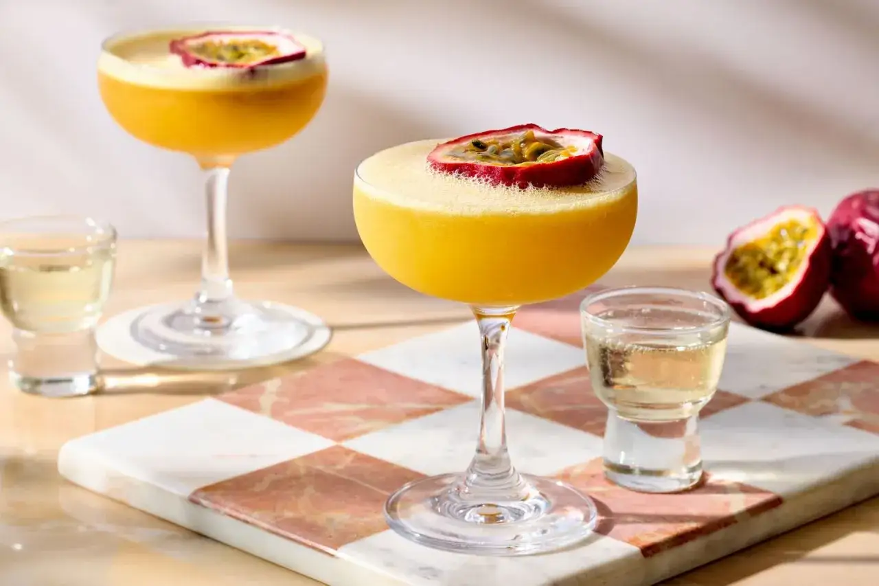 Tv&aring; Pornstar Martini-drinkar med passionsfrukt, en shot och passionsfrukter p&aring; en marmorerad bricka.