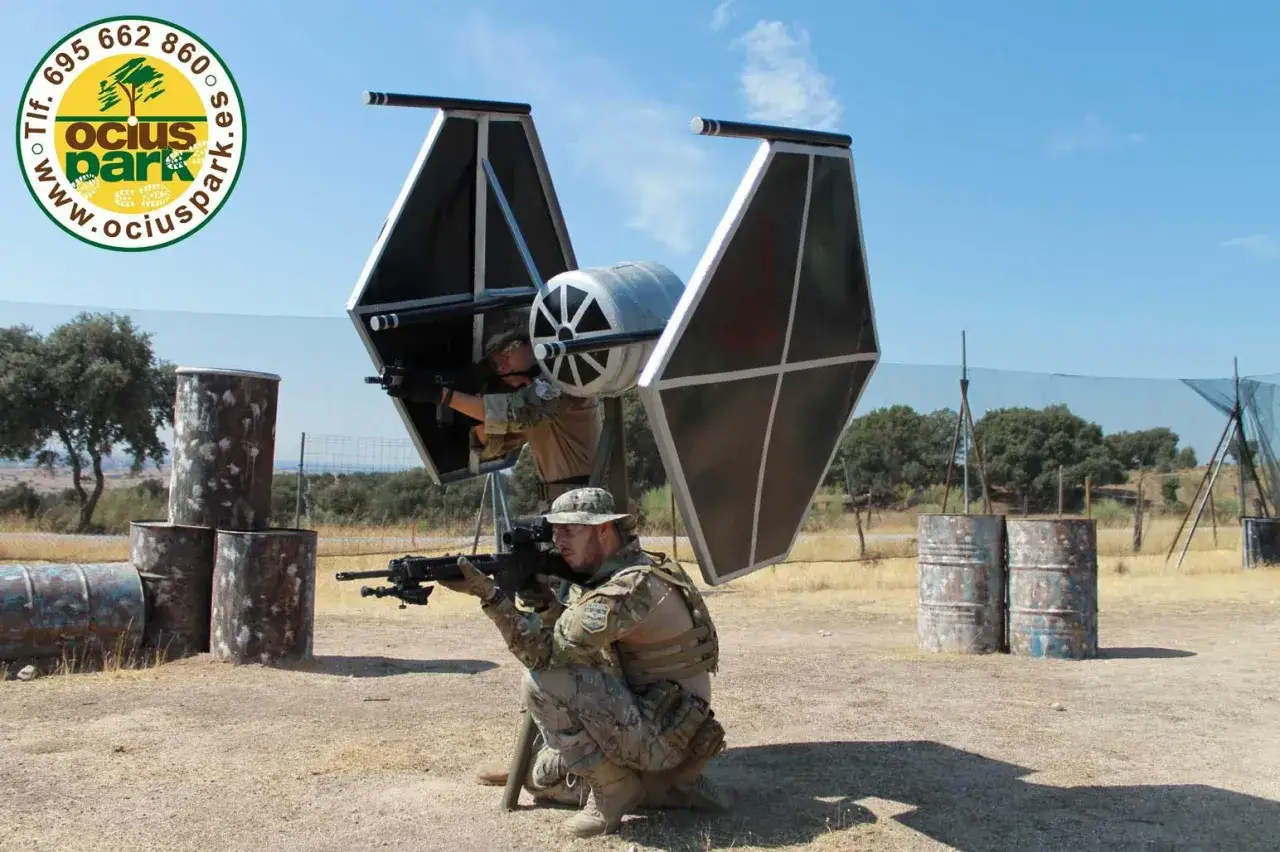 Dos jugadores de airsoft, uno agachado y otro en una estructura, apuntan con sus r&eacute;plicas de armas. &iexcl;As&iacute; es que es airsoft!