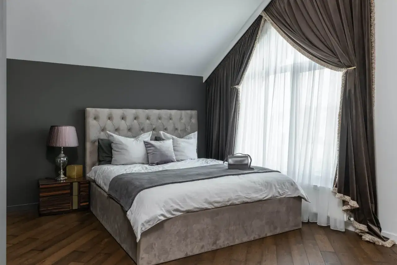 Elegancka sypialnia z szarymi ścianami. Jaki kolor rolet pasuje do szarych ścian? W tym wnętrzu świetnie sprawdziłyby się ciemnobrązowe zasłony.