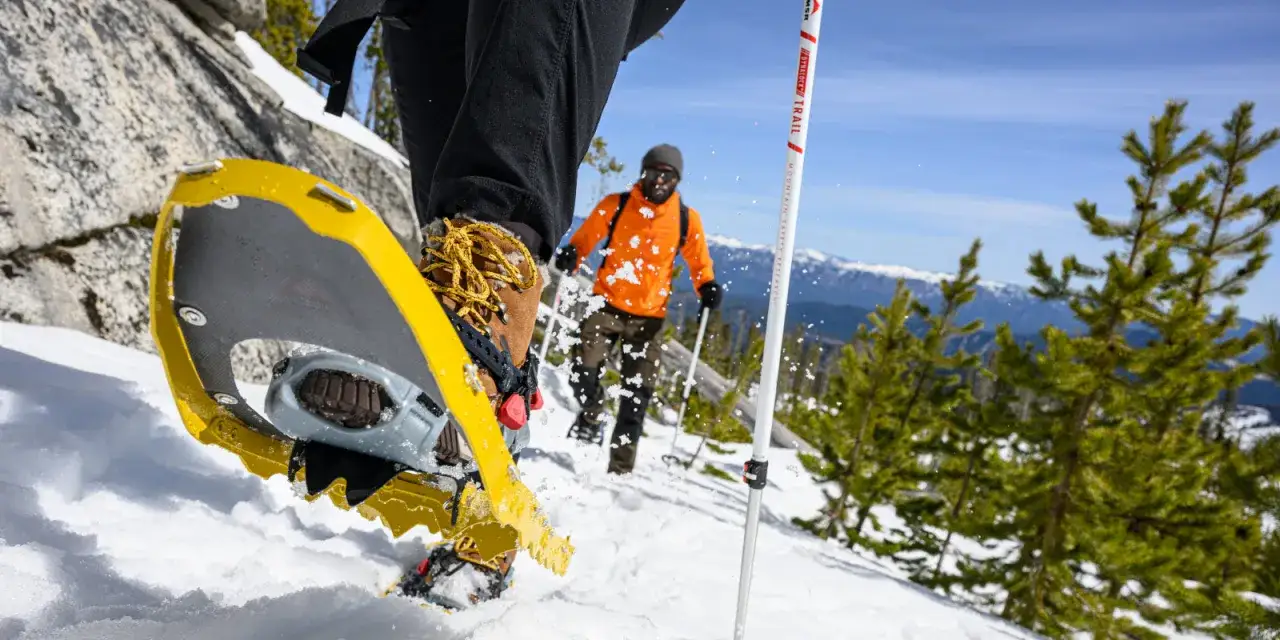 Senderismo invernal con distintos tipos de raquetas de nieve. Un hombre con chaqueta naranja y bastones avanza por la nieve.