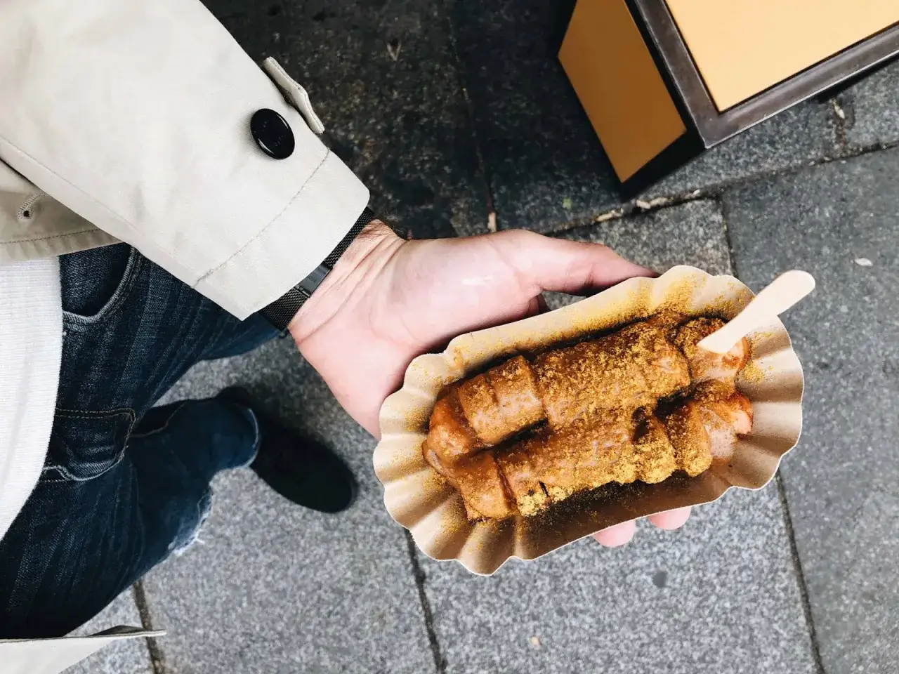 Co zjesc w Dreźnie? Currywurst w papierowym opakowaniu, posypany przyprawami, trzymany w dłoni.
