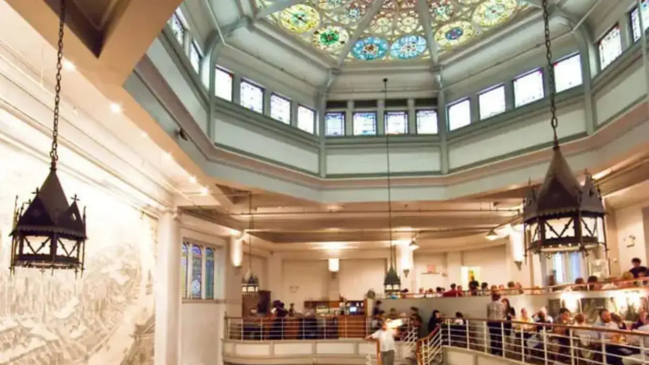 Interior de una iglesia con vitrales en el techo y lámparas góticas. Gente reunida, quizás en una misa gospel en Nueva York.