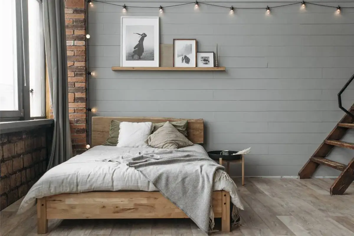 Ideas para un dormitorio acogedor: cama de madera, mantas grises, cuadros en la pared y luces c&aacute;lidas.
