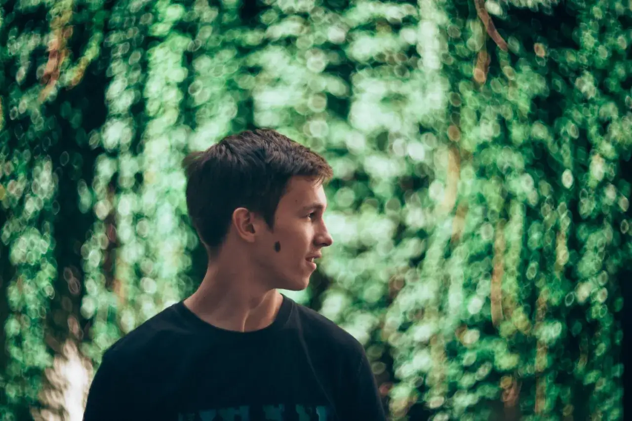 Un jeune homme au grain de beaut&eacute; sur la joue, regardant &agrave; droite, dans un bokeh portrait verdoyant.