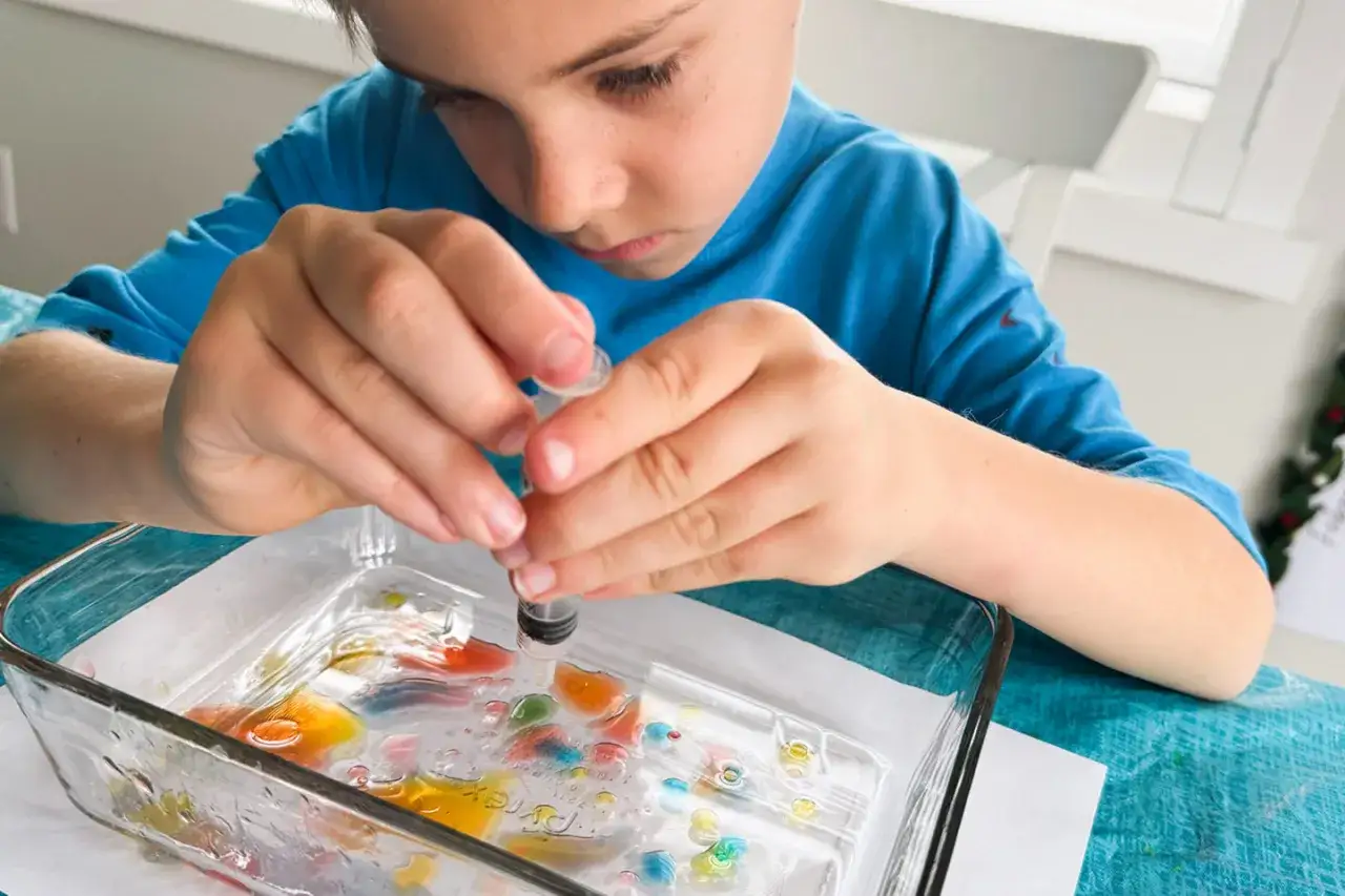 Ni&ntilde;o concentrado realizando experimentos con agua y colorantes en una bandeja de vidrio.