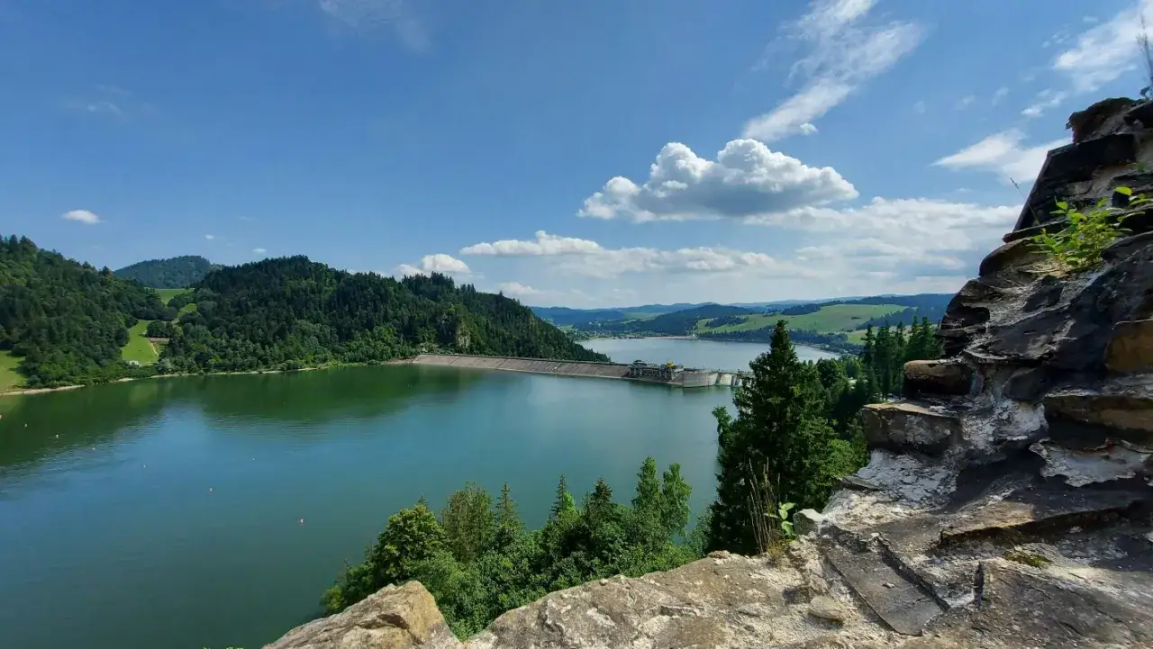 Malownicze jezioro w górach, otoczone zielonymi lasami, z tamą w tle.