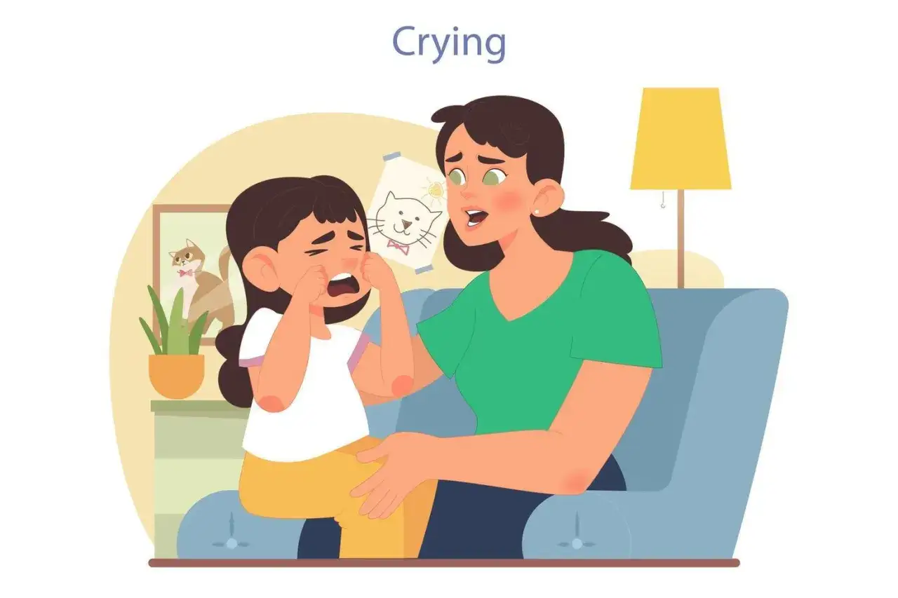 Ni&ntilde;a llora desconsoladamente, mostrando frustraci&oacute;n emocional. Su madre intenta consolarla sentada en un sof&aacute; azul, con un cuadro de un gato y una l&aacute;mpara de fondo.