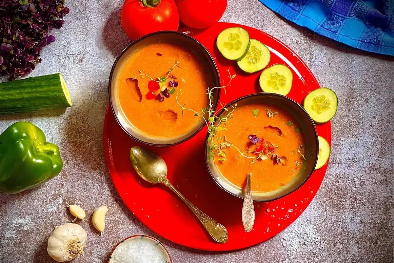 Zwei Schalen mit erfrischendem Gazpacho, garniert mit Kr&auml;utern und Bl&uuml;ten. Zutaten wie Tomaten, Gurke, Paprika und Knoblauch deuten auf ein k&ouml;stliches Gazpacho Rezept hin.